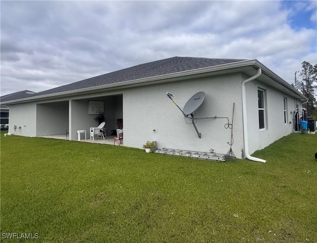 rear view of house featuring roof with shingles, a patio area, a lawn, and stucco siding