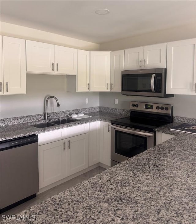 kitchen featuring dark stone countertops, white cabinetry, appliances with stainless steel finishes, and a sink