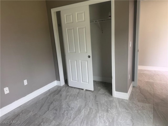 unfurnished bedroom with a closet, marble finish floor, and baseboards