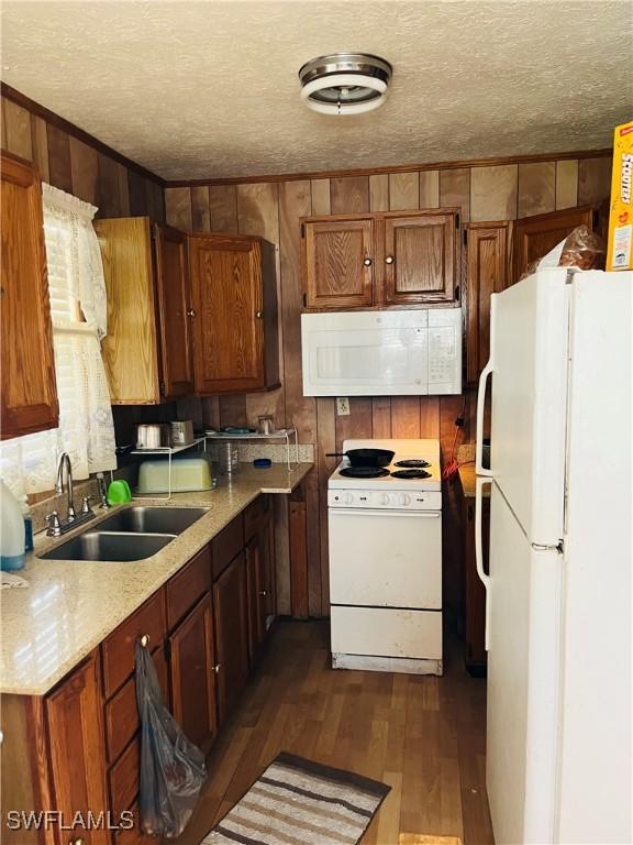 kitchen featuring white appliances, sink, wood walls, a textured ceiling, and dark wood-type flooring