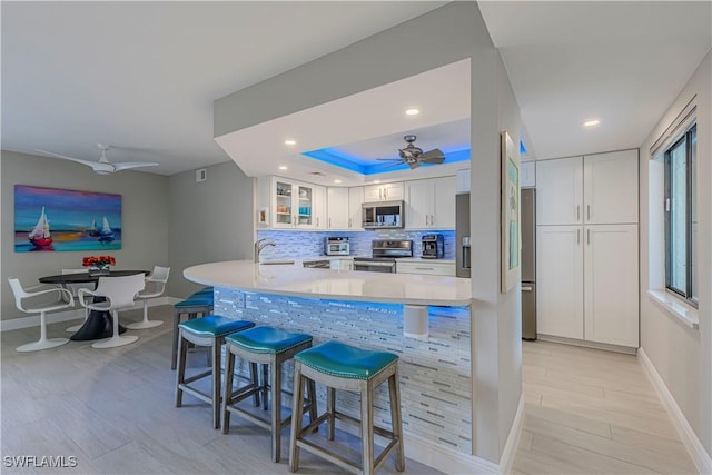 kitchen with stainless steel appliances, tasteful backsplash, white cabinetry, a sink, and a kitchen breakfast bar