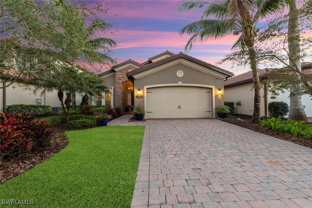 mediterranean / spanish-style home with a garage, a yard, a tiled roof, decorative driveway, and stucco siding