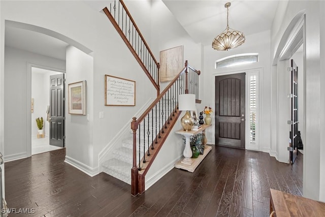 foyer with arched walkways, hardwood / wood-style floors, baseboards, and stairway