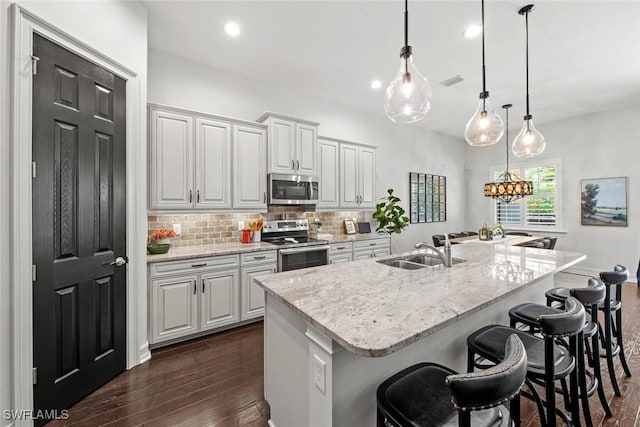 kitchen featuring a kitchen breakfast bar, dark wood-style floors, stainless steel appliances, backsplash, and a sink