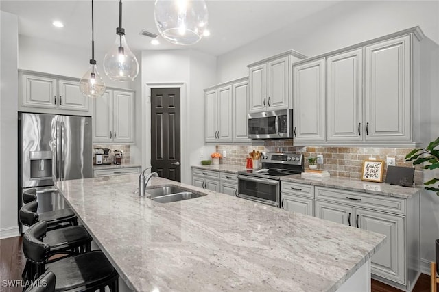 kitchen featuring light stone counters, a sink, decorative backsplash, an island with sink, and appliances with stainless steel finishes