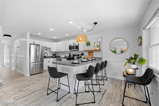 kitchen featuring a peninsula, a breakfast bar, white cabinetry, appliances with stainless steel finishes, and dark countertops