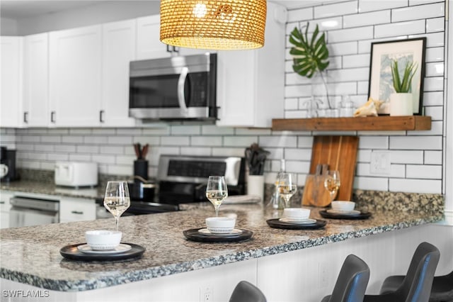 kitchen featuring stone counters, stainless steel appliances, decorative backsplash, white cabinetry, and a peninsula