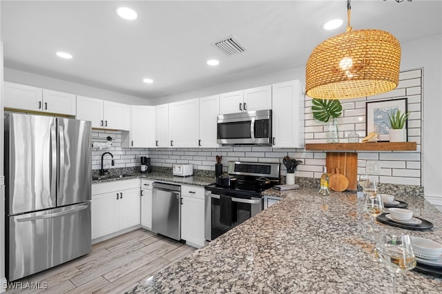 kitchen with pendant lighting, stainless steel appliances, white cabinetry, a sink, and dark stone counters