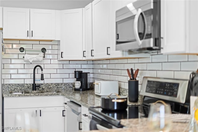 kitchen with stainless steel appliances, white cabinetry, a sink, and light stone countertops