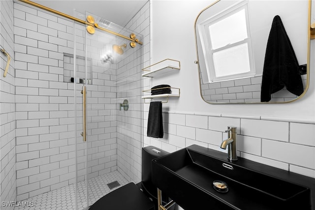 full bath with a wainscoted wall, a sink, visible vents, tile walls, and a shower stall