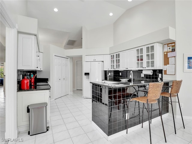 kitchen featuring white refrigerator with ice dispenser, white cabinetry, decorative backsplash, a kitchen bar, and glass insert cabinets