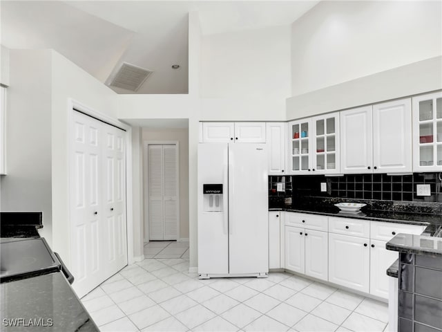 kitchen featuring visible vents, glass insert cabinets, white cabinets, dark stone countertops, and white fridge with ice dispenser