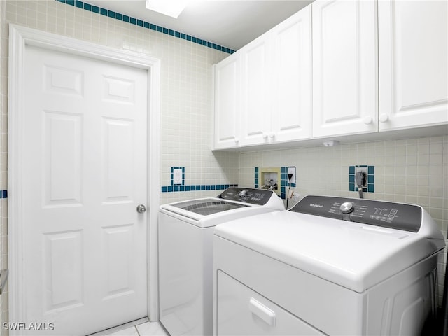 laundry area featuring separate washer and dryer, cabinet space, and tile walls