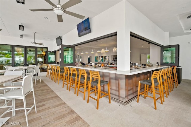 bar featuring a community bar, a healthy amount of sunlight, ceiling fan, and light wood finished floors