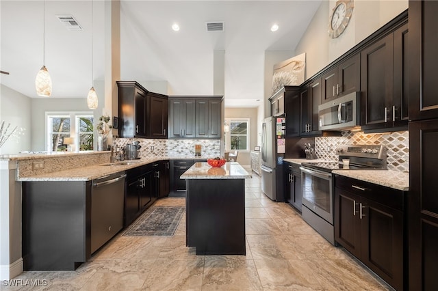 kitchen with a peninsula, a kitchen island, visible vents, appliances with stainless steel finishes, and decorative light fixtures