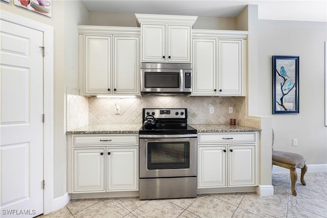 kitchen featuring light tile patterned floors, tasteful backsplash, appliances with stainless steel finishes, light stone counters, and white cabinetry