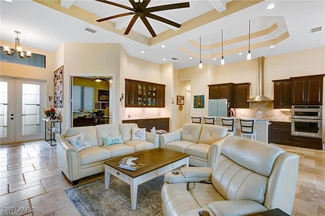 living room with french doors, a high ceiling, a raised ceiling, crown molding, and ceiling fan with notable chandelier