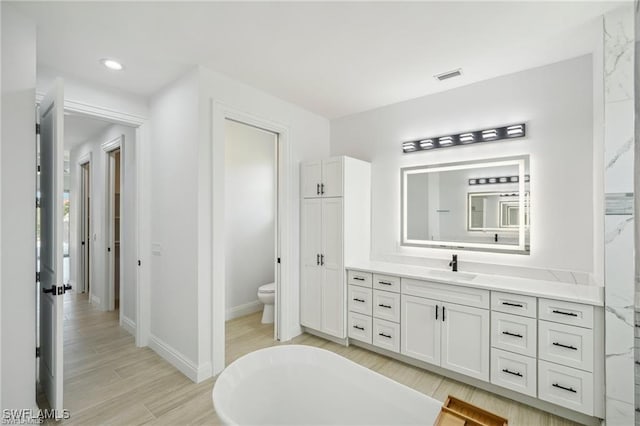 full bathroom featuring toilet, wood finished floors, vanity, visible vents, and baseboards