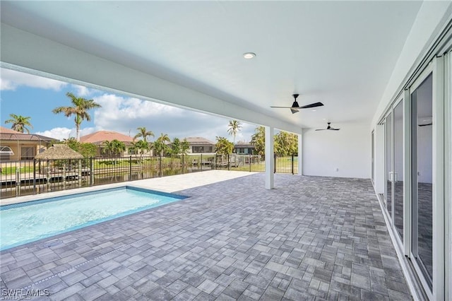 view of swimming pool featuring a patio area, ceiling fan, a water view, and fence