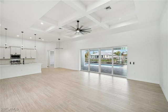 unfurnished living room featuring ceiling fan, a towering ceiling, visible vents, light wood-style floors, and beam ceiling