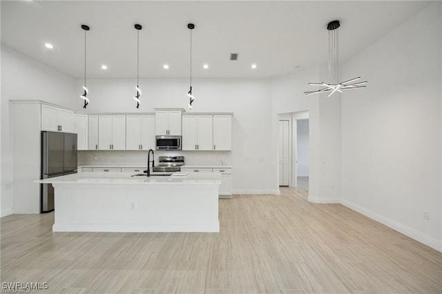 kitchen with white cabinets, an island with sink, hanging light fixtures, stainless steel appliances, and light countertops