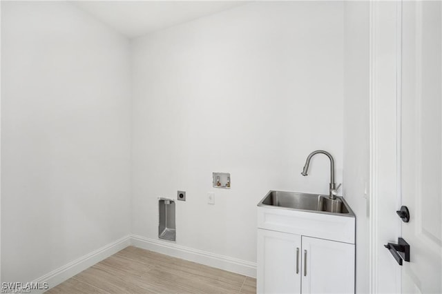 washroom featuring cabinet space, baseboards, light wood-style flooring, hookup for a washing machine, and a sink