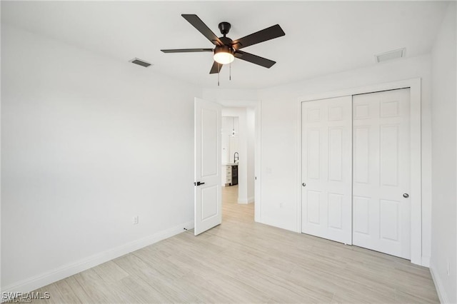 unfurnished bedroom featuring light wood-style flooring, a closet, visible vents, and baseboards