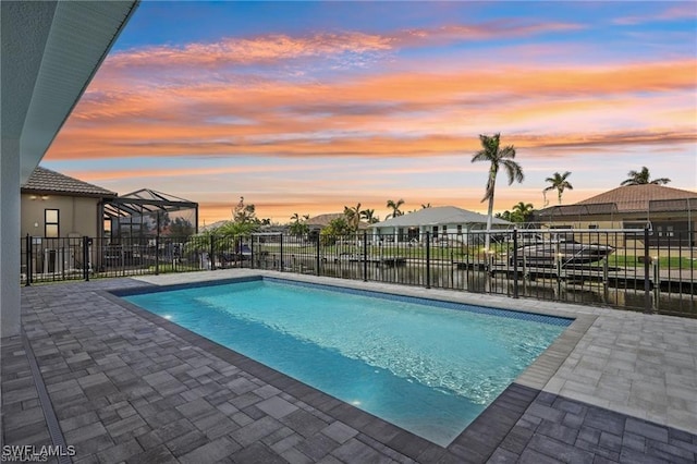 pool at dusk with a lanai, a patio area, fence, and a fenced in pool