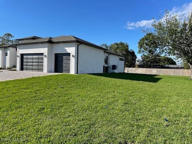 view of side of property featuring fence, stucco siding, decorative driveway, a yard, and a garage