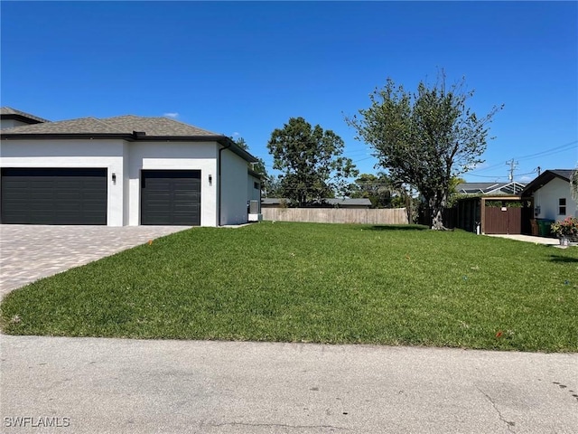 view of yard with decorative driveway, an attached garage, and fence