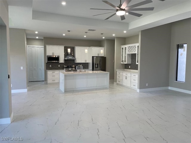 kitchen featuring baseboards, decorative backsplash, appliances with stainless steel finishes, marble finish floor, and wall chimney exhaust hood