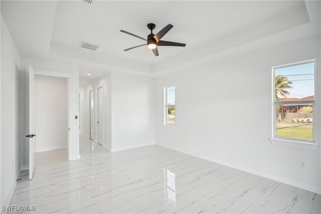 unfurnished room featuring ceiling fan, visible vents, baseboards, marble finish floor, and a tray ceiling