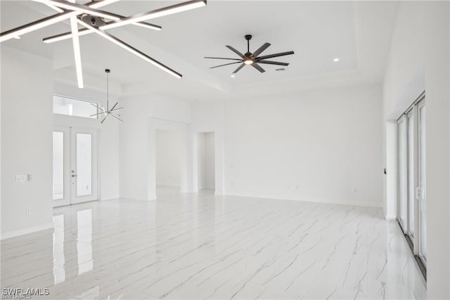 empty room with ceiling fan with notable chandelier, baseboards, marble finish floor, french doors, and a tray ceiling