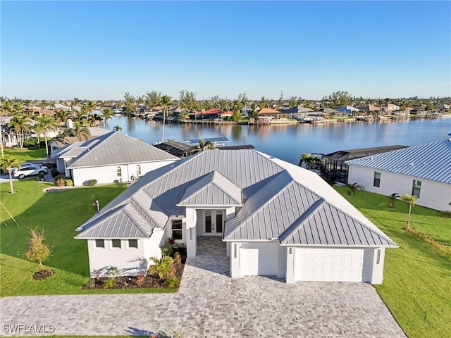 modern inspired farmhouse with metal roof, an attached garage, a water view, decorative driveway, and a standing seam roof