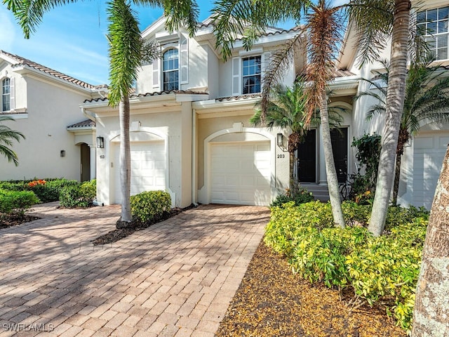 mediterranean / spanish home featuring driveway, an attached garage, a tiled roof, and stucco siding