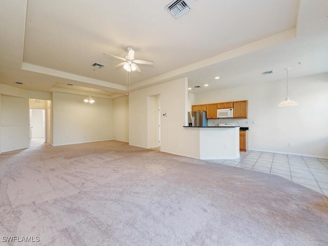 unfurnished living room featuring a tray ceiling, light colored carpet, and visible vents