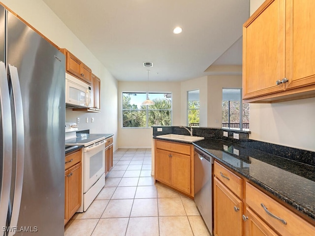 kitchen featuring light tile patterned flooring, stainless steel appliances, a sink, hanging light fixtures, and dark stone counters