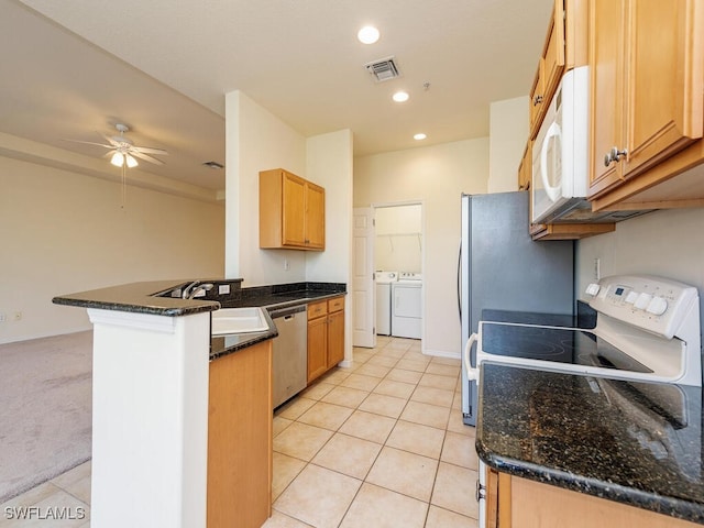 kitchen with white appliances, light tile patterned floors, dark stone countertops, a peninsula, and washer and dryer