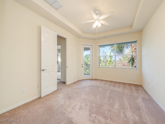 empty room featuring baseboards, ceiling fan, a tray ceiling, and light colored carpet