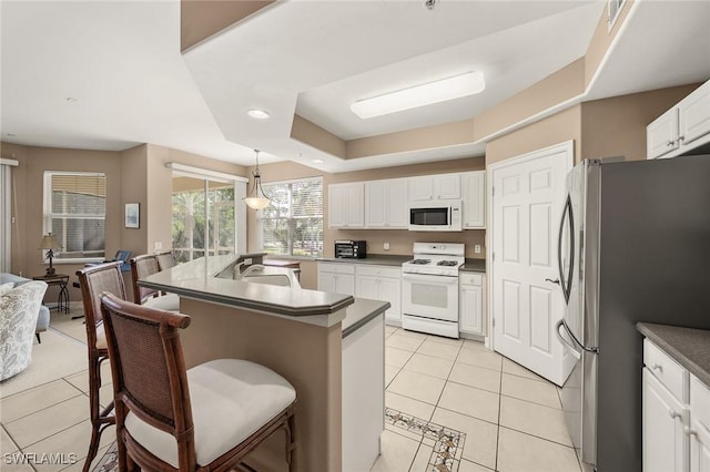 kitchen with white appliances, a breakfast bar area, dark countertops, and white cabinets