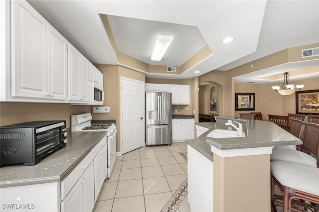 kitchen featuring white appliances, a kitchen breakfast bar, a tray ceiling, white cabinetry, and a sink