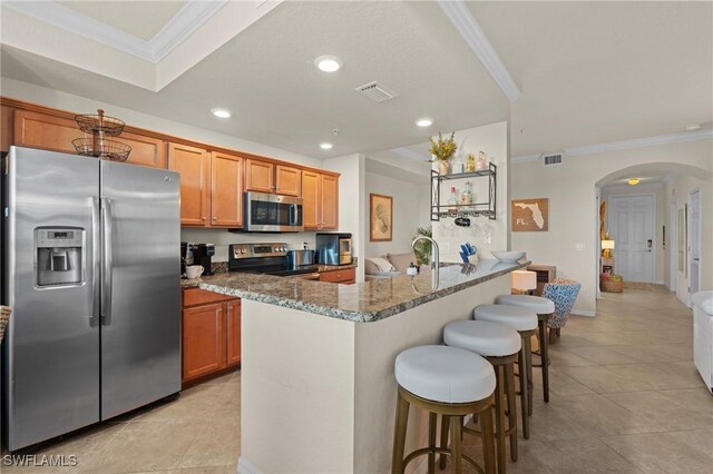 kitchen featuring an island with sink, stone countertops, arched walkways, and stainless steel appliances