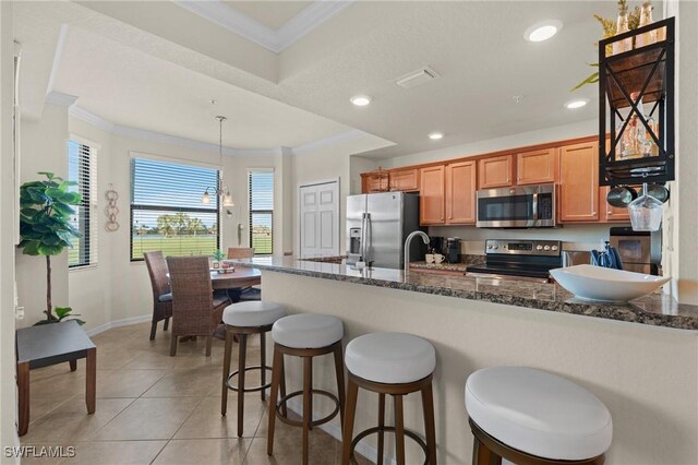 kitchen featuring ornamental molding, hanging light fixtures, appliances with stainless steel finishes, and dark stone counters