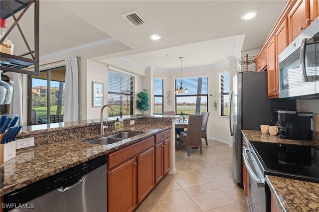 kitchen featuring a sink, appliances with stainless steel finishes, dark stone counters, decorative light fixtures, and crown molding