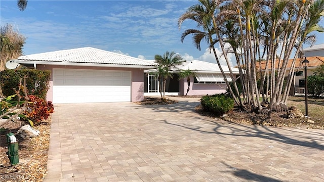 single story home with a tiled roof, decorative driveway, an attached garage, and stucco siding