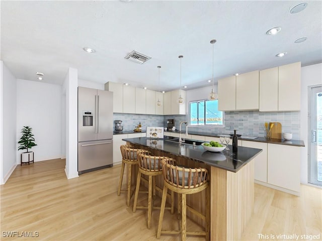 kitchen featuring dark countertops, stainless steel fridge, a breakfast bar area, and light wood-style flooring