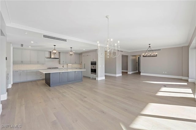 kitchen with a center island with sink, a chandelier, pendant lighting, and wall chimney range hood