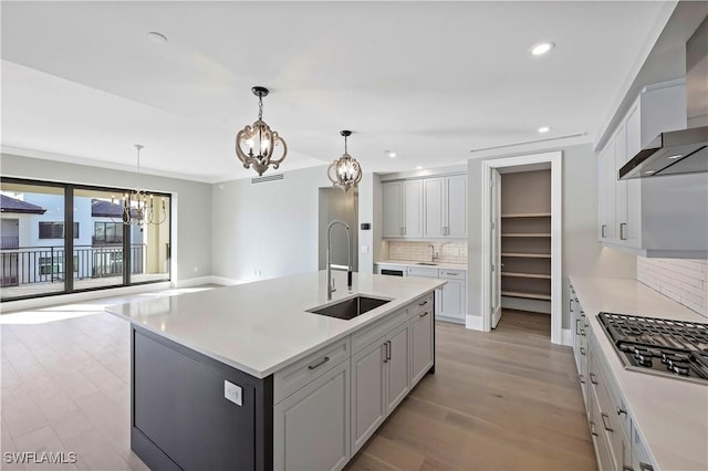 kitchen with a notable chandelier, stainless steel gas stovetop, pendant lighting, sink, and a kitchen island with sink