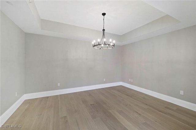 unfurnished room featuring light wood-type flooring, a chandelier, and a raised ceiling