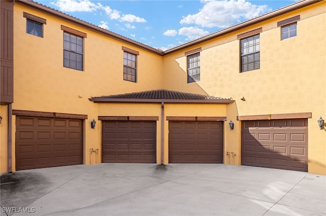 townhome / multi-family property with an attached garage, driveway, a tiled roof, and stucco siding